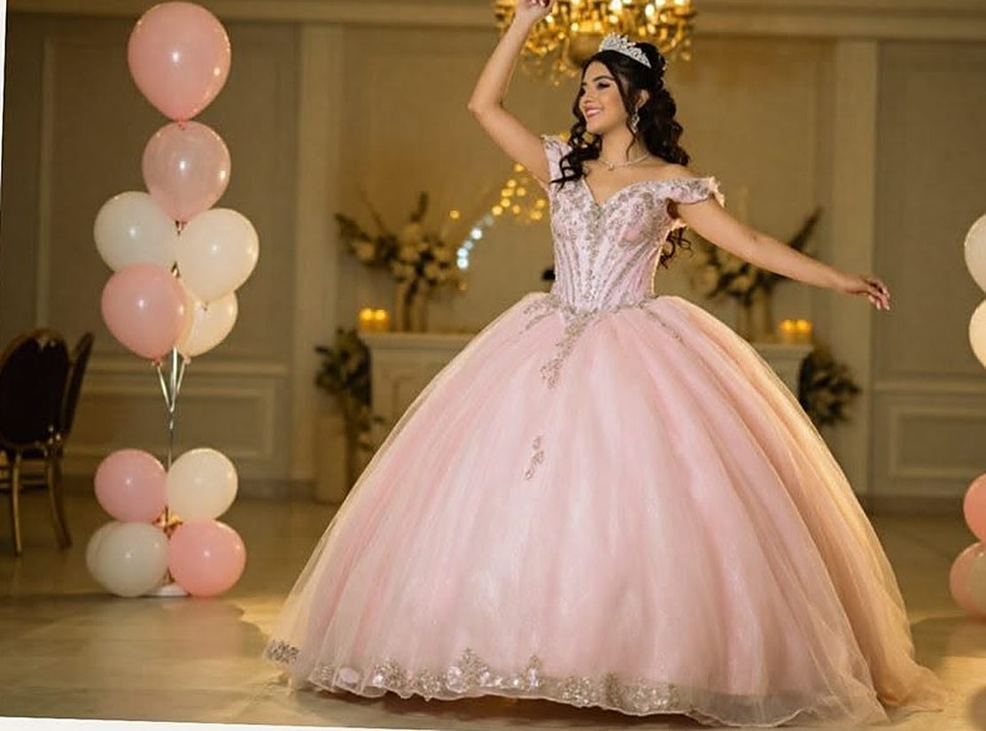 Quinceañera con vestido rosa bailando entre globos en un salón de fiestas